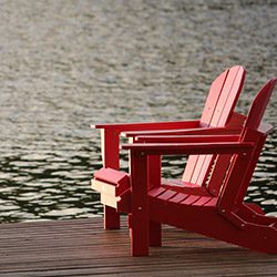 Two Adirondack chairs on a dock near the water