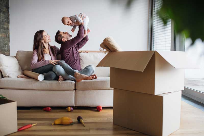 A portrait of young couple with a baby and cardboard boxes moving in a new home in Port Huron, MI 